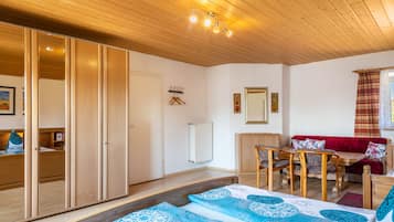 Ein gemütliches Zimmer mit Holzbalkendecke, einem Bett mit gemusterten Textilien, einem roten Sofa, einem Holztisch und einer Heizung.