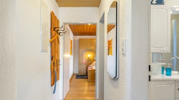 Un couloir avec des patères en bois fixées au mur, un miroir et une salle de bain équipée d’un lavabo et de produits de toilette.