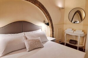 A bed with a headboard, pillows, a bedside table with a mirror, and a wall-mounted shelf with towels. - Among the historic alleys of Rome (Domus Viola) (Roma)