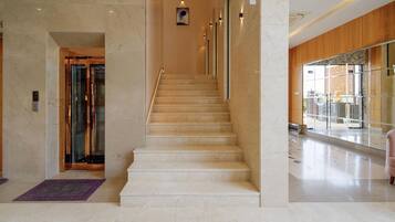 A marble staircase in a hotel lobby with a glass elevator and a view of the outside.