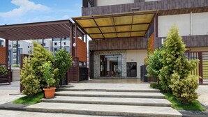 Una entrada moderna a un edificio con un vestíbulo cubierto, escalones que conducen a la puerta y plantas en macetas a ambos lados.