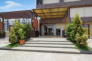 Una entrada moderna a un edificio con un vestíbulo cubierto, escalones que conducen a la puerta y plantas en macetas a ambos lados.