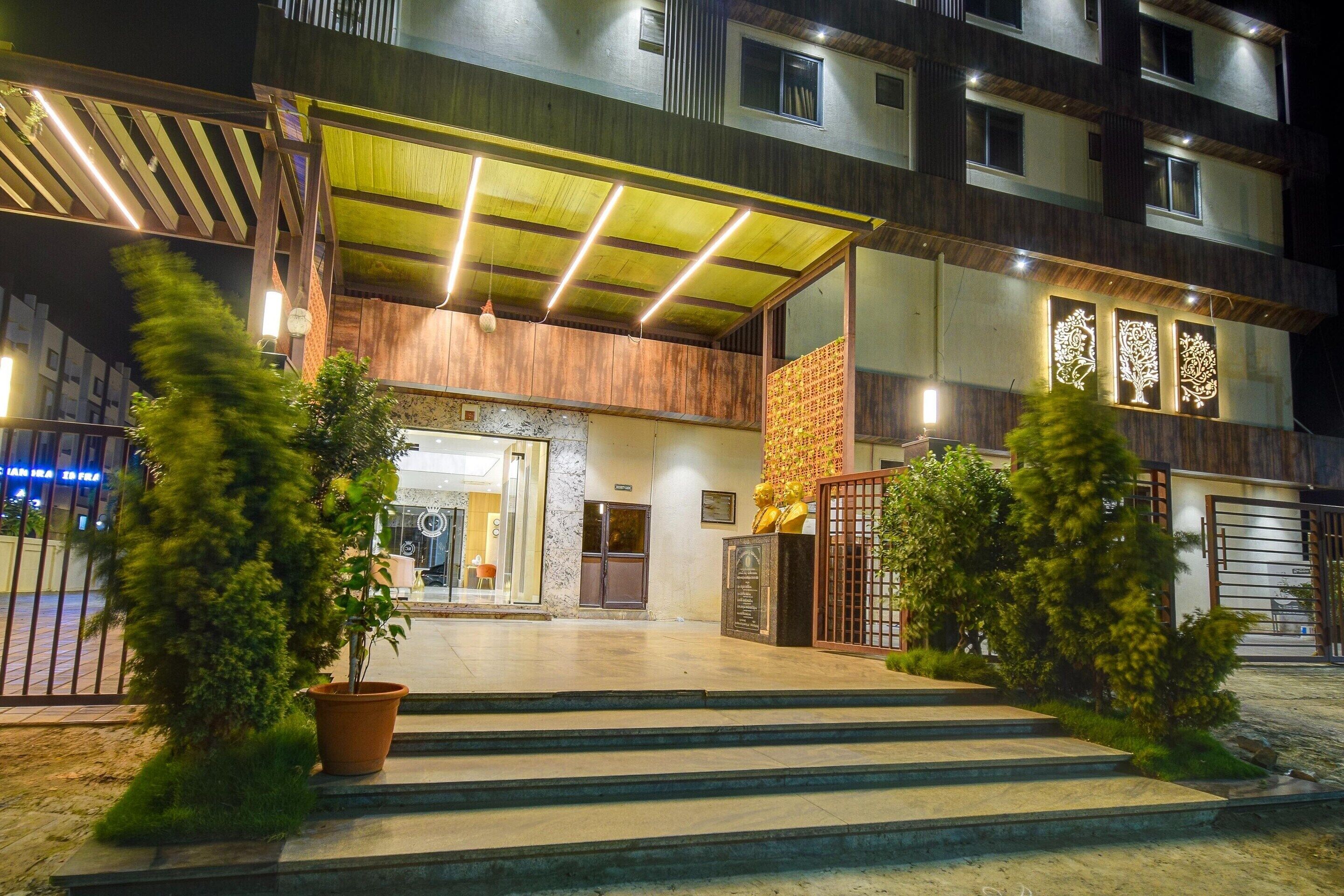 Un hôtel à plusieurs étages doté d’une entrée couverte, de plantes en pot et d’une allée d’accès fermée par un portail.