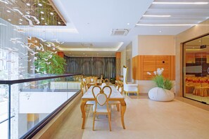 A dining area with a long table and chairs, a potted plant, and a view of the outside through a glass wall.