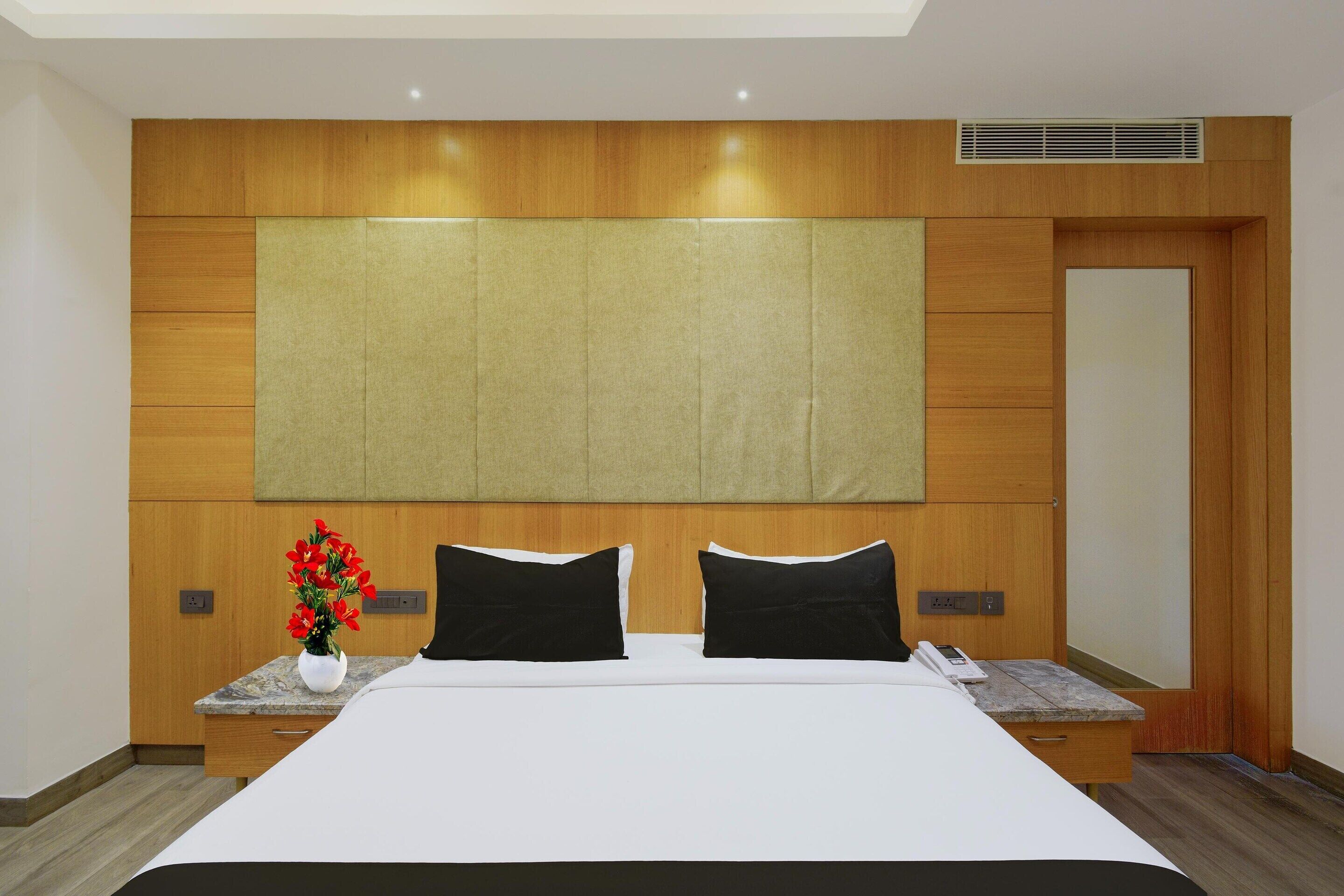 Une chambre d’hôtel avec un grand lit, une tête de lit en bois, des tables de chevet et un panneau de commande fixé au mur.