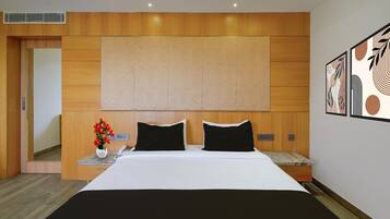 A modern hotel room with a large bed, wooden headboard, a nightstand with a vase of flowers, and a wall-mounted artwork.