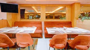 Un restaurante con paneles de madera, asientos tipo cabina acolchados en naranja y un televisor de pantalla plana montado en la pared.
