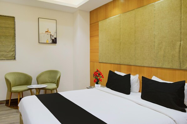 Une chambre d’hôtel avec un lit, deux chaises, une petite table, un tableau et un vase de fleurs.