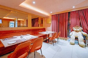 A restaurant with a booth seating area, a large teddy bear decoration, and a counter with a beverage dispenser. - Palette Rc Platinum Hotel (Mahabubabad)