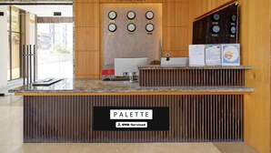 Un mostrador de recepción con un cartel que dice 'RECEPTION', un reloj con múltiples zonas horarias, una computadora y un cartel que dice 'PALETTE'.