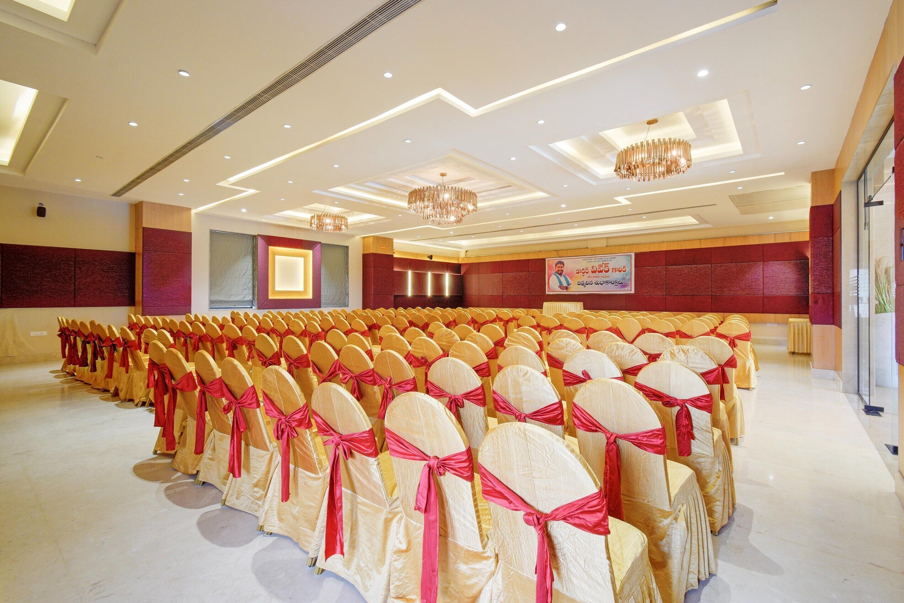A conference room with rows of chairs, a chandelier, and a banner on the wall.