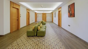 Un pasillo de hotel con alfombra estampada, un sofá verde con cojines, puertas de madera y un ventilador de techo.