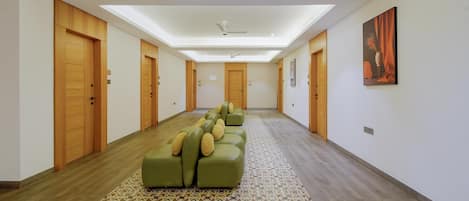 A hotel hallway with a patterned carpet, a green sofa with cushions, wooden doors, and a ceiling fan.