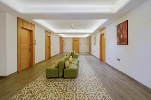 Un pasillo de hotel con alfombra estampada, un sofá verde con cojines, puertas de madera y un ventilador de techo.