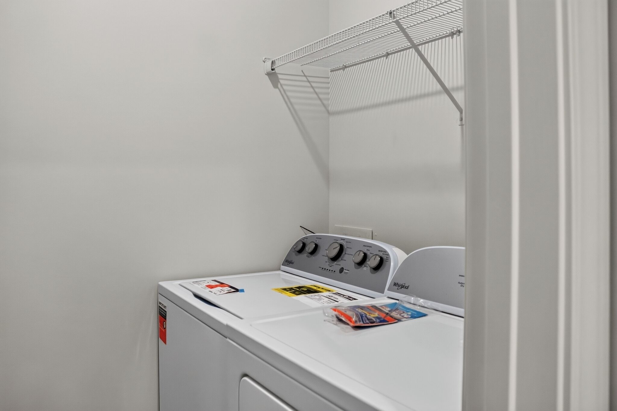 A white laundry room with a Whirlpool washer and dryer, a metal drying rack, and a door with a handle.