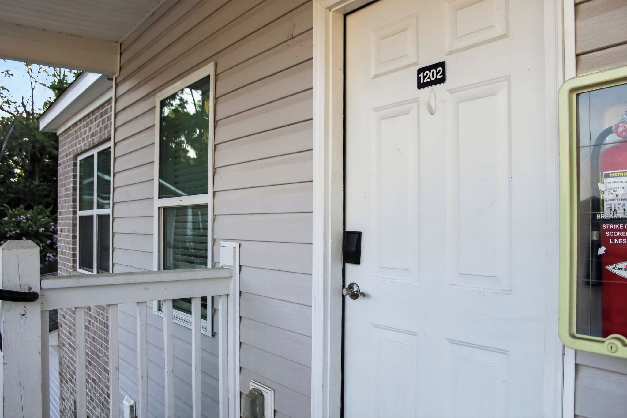 A house with a white door marked '1202,' a small porch, and a window with a fire extinguisher.