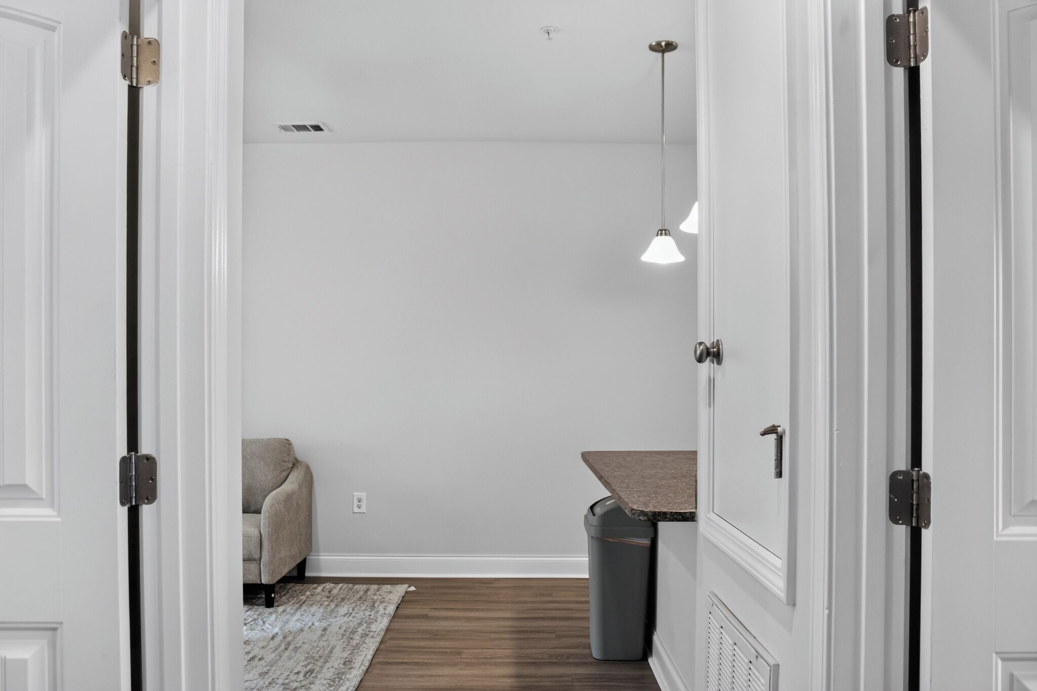 Un couloir aux murs blancs, une poubelle grise, un canapé gris et une suspension.
