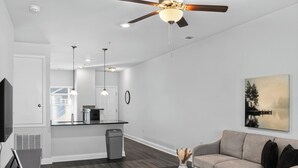 Un soggiorno moderno con ventilatore a soffitto, un divano, un tavolino da caffè e una cucina sullo sfondo.