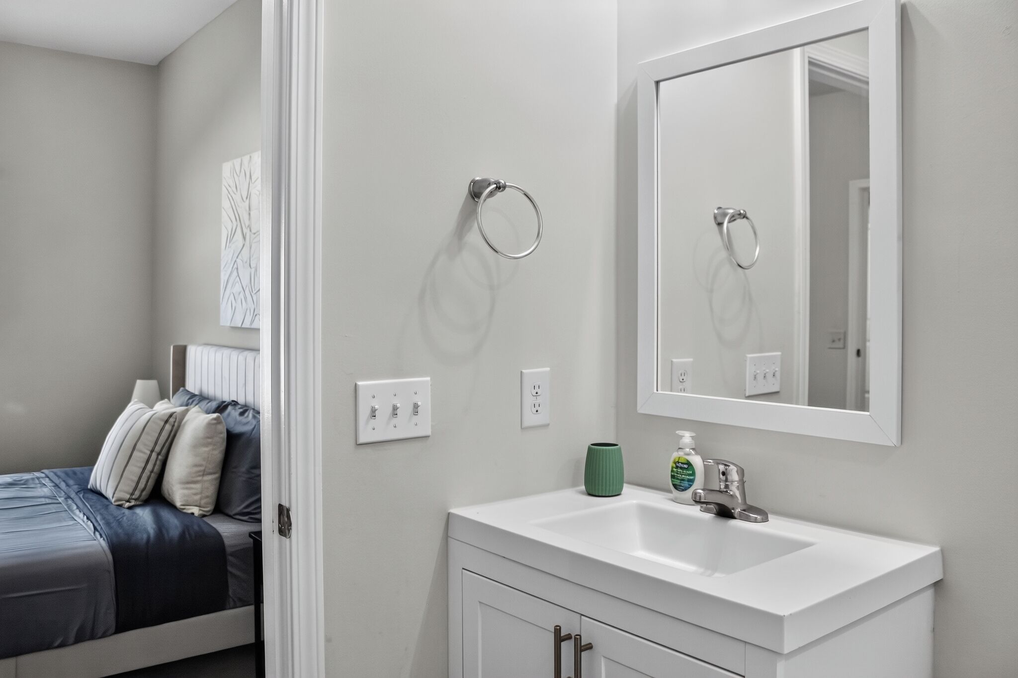 A modern bathroom with a white sink, mirror, and towel rings.