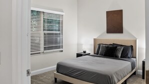 Ein Schlafzimmer mit einem Bett, einem Nachttisch, einem Fenster mit Jalousien und einem Wandbild.