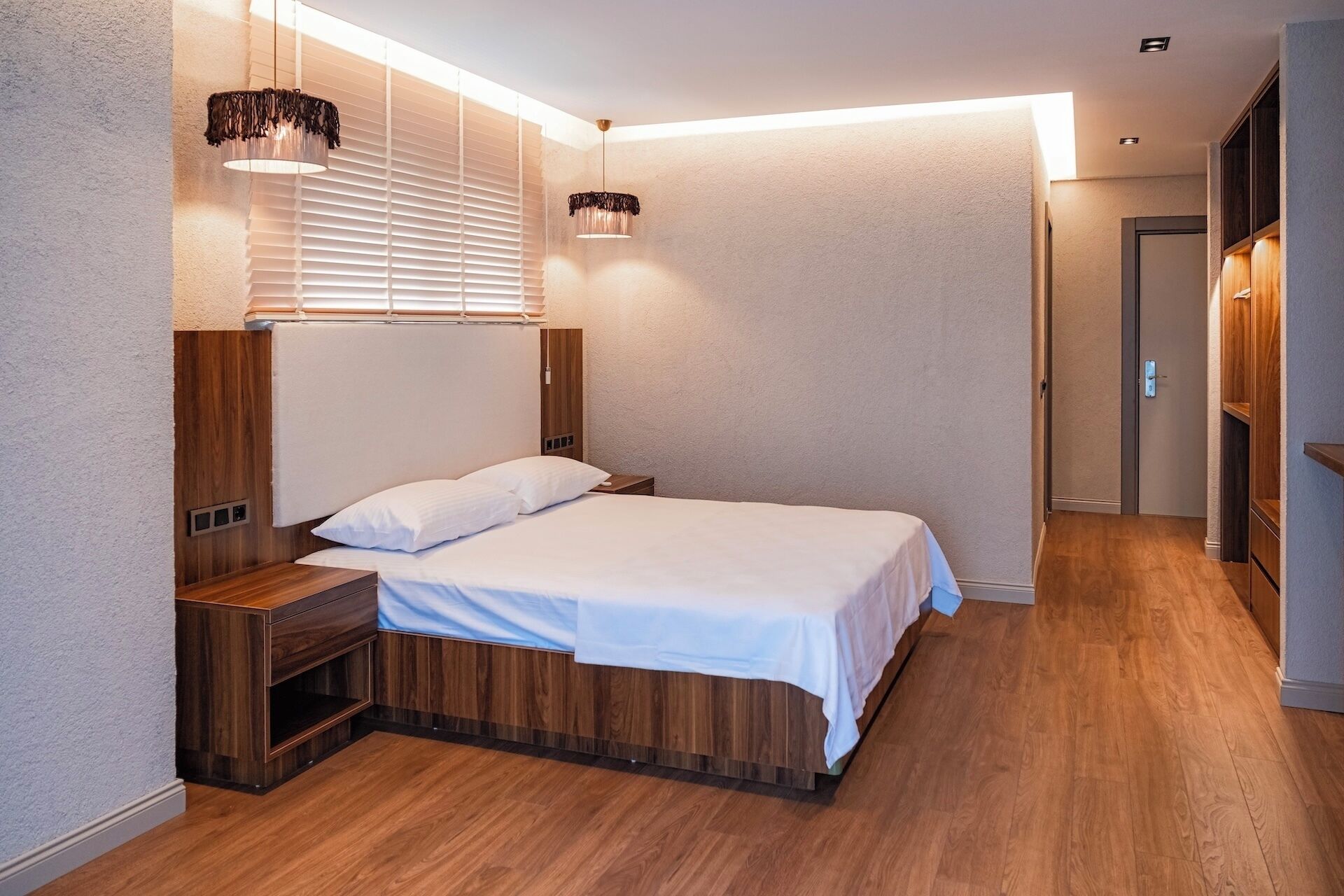 Un dormitorio moderno con estructura de cama de madera, una mesita de noche, una lámpara de pared y un armario empotrado.