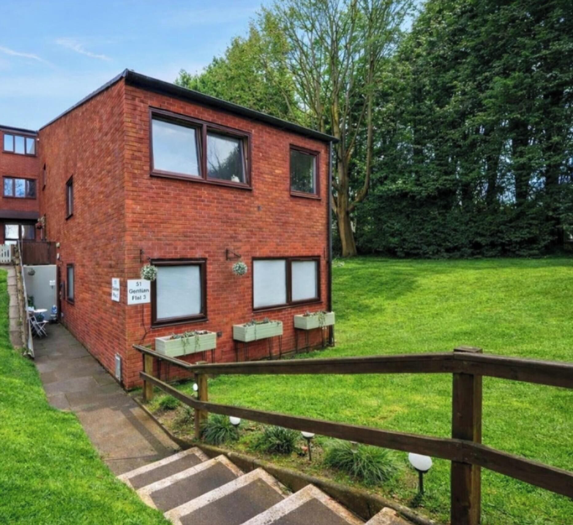 A red brick building with a small front yard, a wooden staircase, and a sign indicating 'Gentleman Flat 5'.