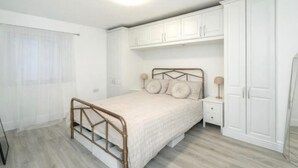 Une chambre à coucher comprenant un lit, une armoire, une table de chevet et une fenêtre avec des rideaux légers.