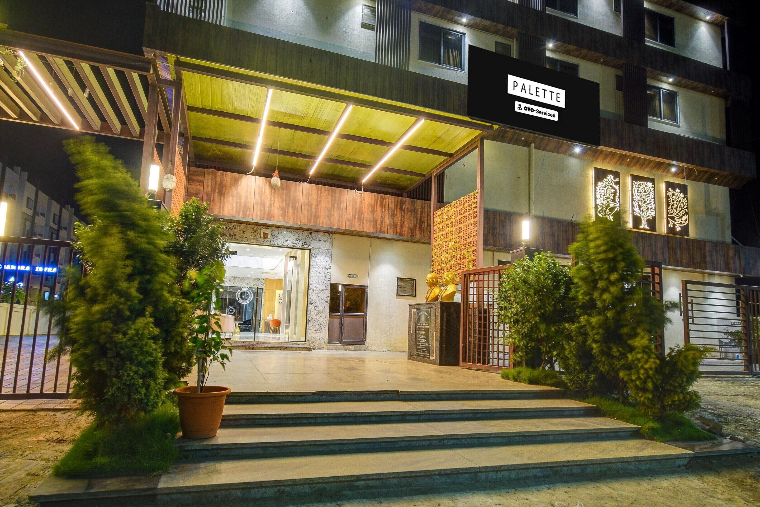Entrada de hotel con un vestíbulo cubierto, mostrador de recepción y un cartel que indica el nombre 'PALETTE'.