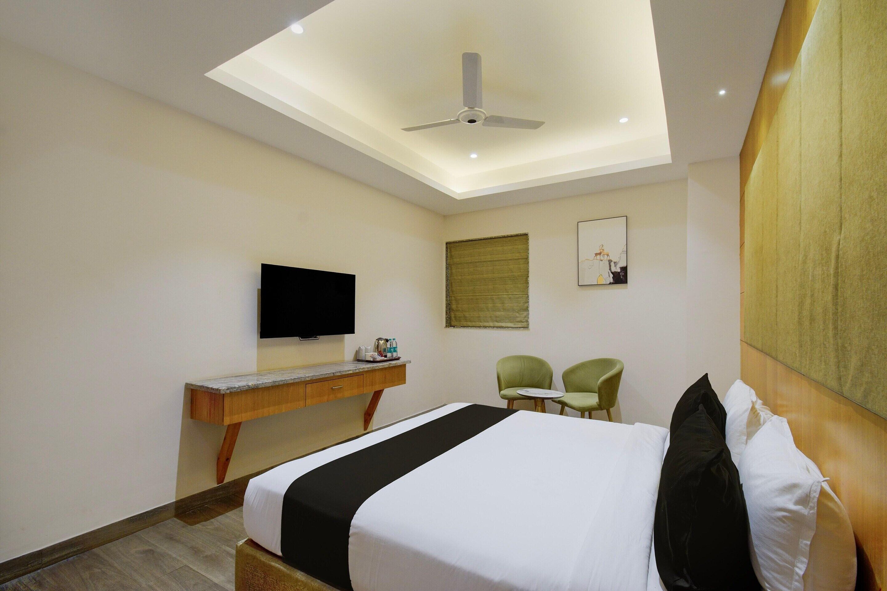 A hotel room with a bed, a desk, a television, two chairs, and a ceiling fan.