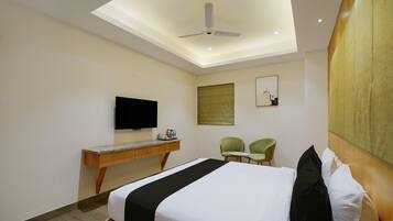 A hotel room with a bed, a desk, a television, two chairs, and a ceiling fan.