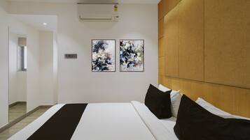 Une chambre d’hôtel avec un lit, deux tableaux abstraits, une tête de lit en bois et un climatiseur fixé au mur.