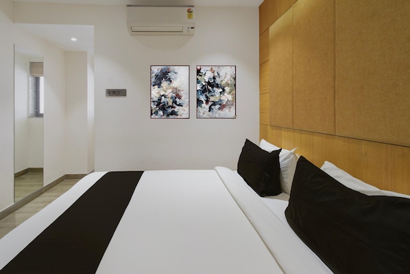 Habitación de hotel con una cama, dos cuadros abstractos, cabecera de madera y aire acondicionado de pared.