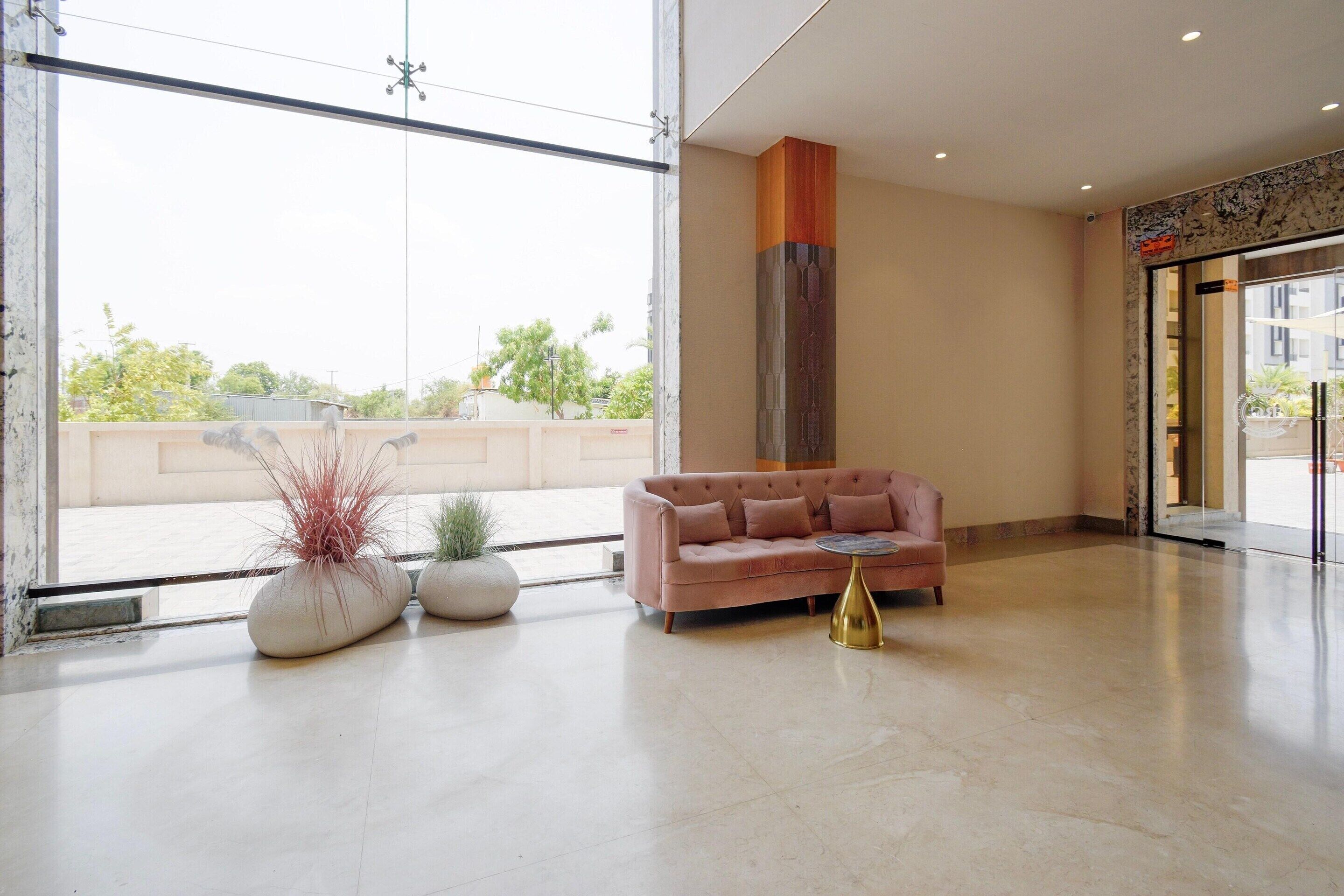 A spacious lobby with a large glass door, a pink sofa, and two potted plants.