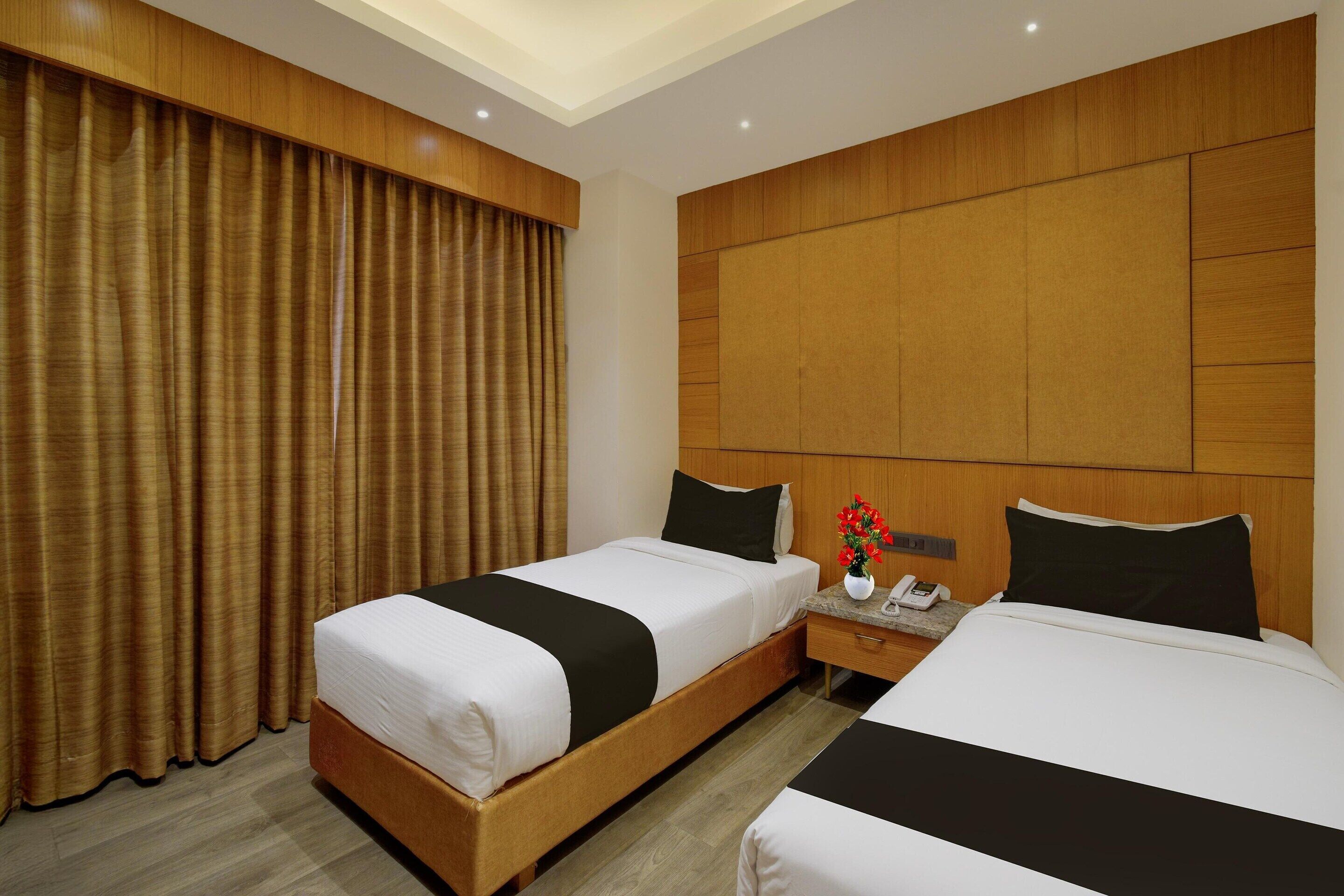 A hotel room with two beds, a wooden headboard, a nightstand with a phone, and a window with curtains.