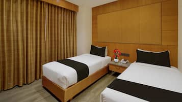 A hotel room with two beds, a wooden headboard, a nightstand with a phone, and a window with curtains.
