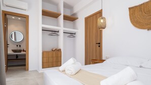 Una habitación de hotel moderna con una cama, un armario de madera, un baño con espejo y una lámpara colgante.