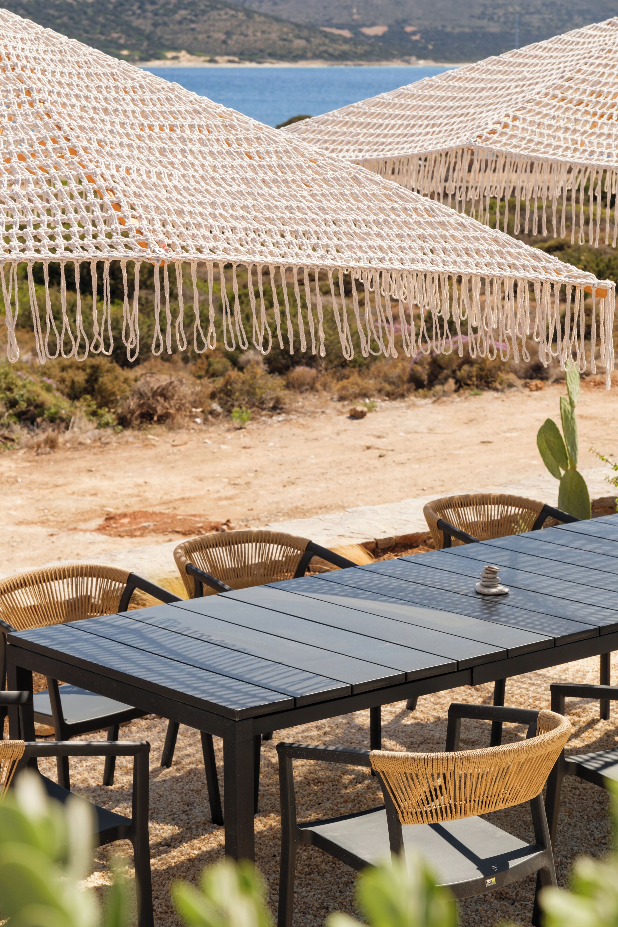 A beachside dining area with tables and chairs, surrounded by macrame umbrellas.
