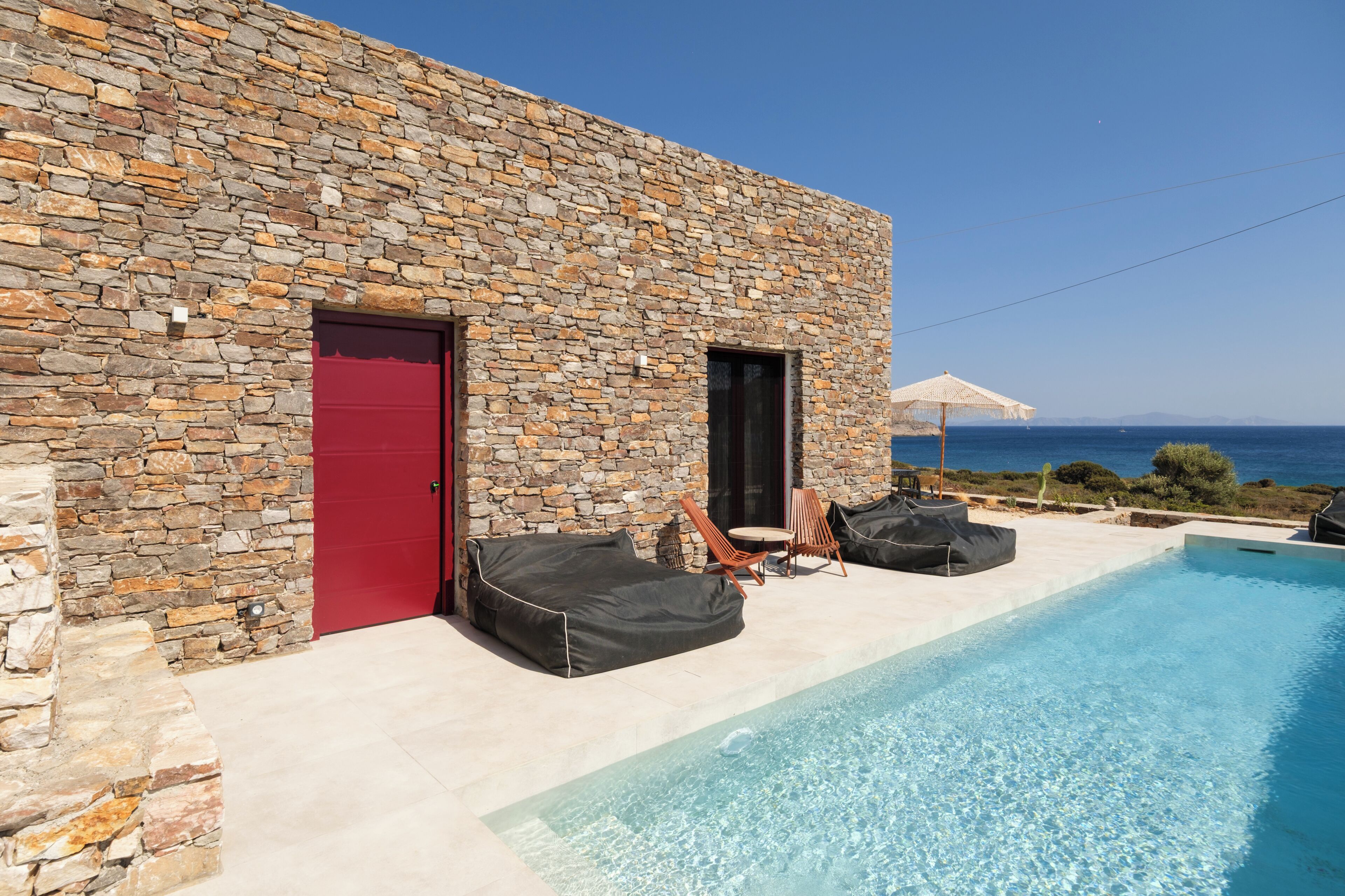 Ein Gebäude aus Stein mit roter Tür, einem Pool und Sitzgelegenheiten im Freien.