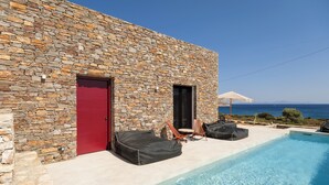 Un edificio de piedra con puerta roja, piscina y mobiliario para exteriores.