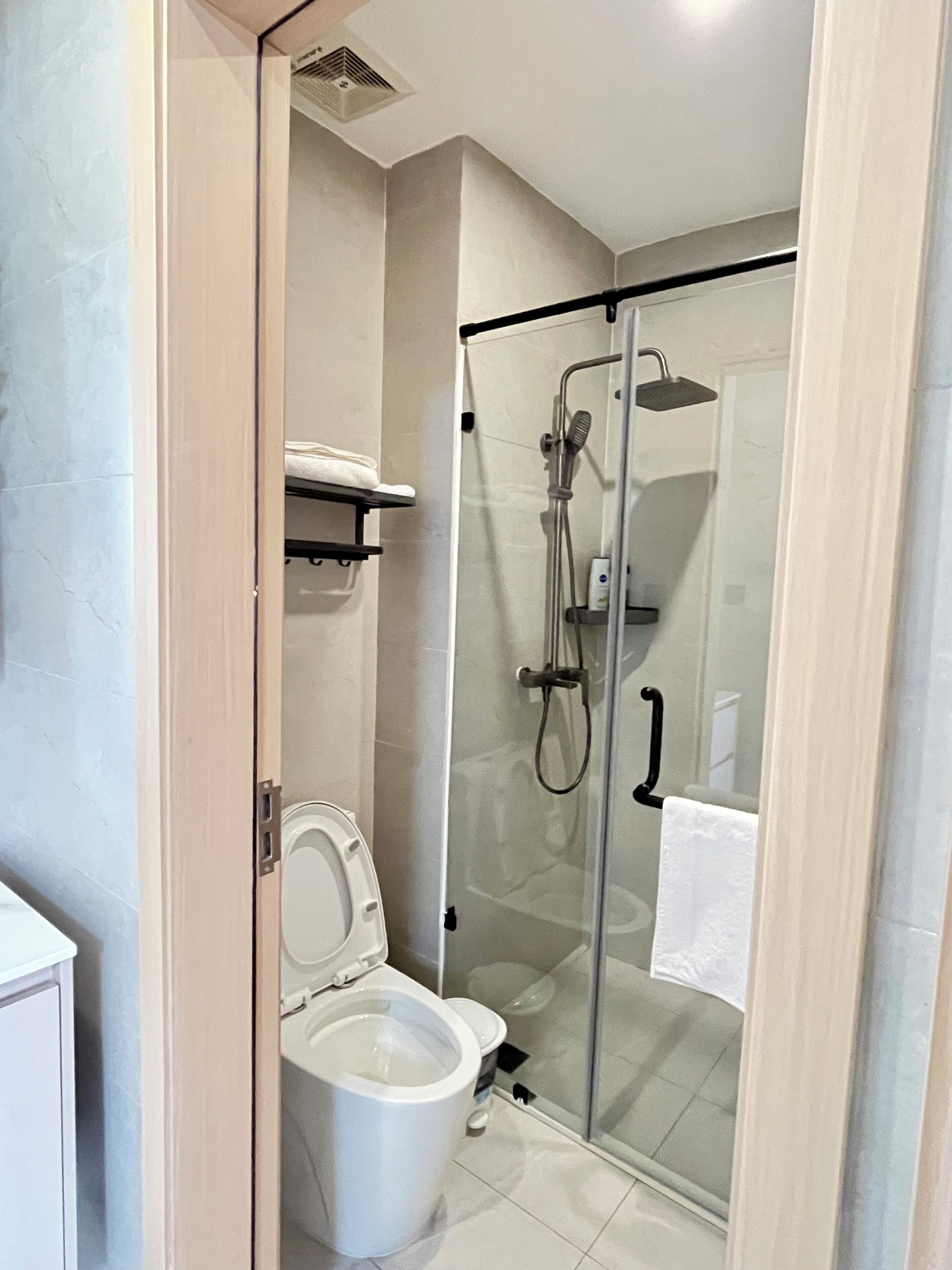 A modern bathroom with a glass-enclosed shower, a toilet, and a towel rack.