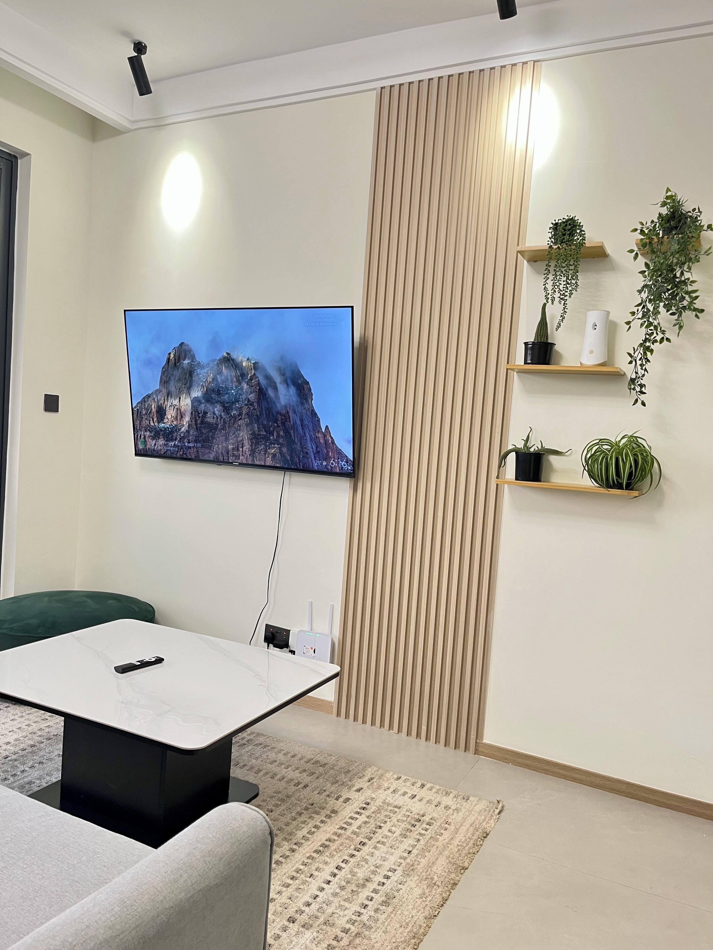 Un saló modern amb televisió de pantalla plana penjada a la paret, un sofà, una taula de centre i una planta decorativa sobre una estant.