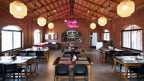 A restaurant with a rustic brick interior, multiple tables and chairs, and a neon sign reading 'The Jungle Kitchen'.