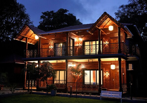 A two-story wooden building with a balcony, large windows, and a well-lit entrance.