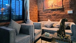 A room with a stone wall, a painting of deer, grey sofas, and a leopard statue.