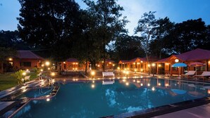 A swimming pool with a surrounding deck, lounge chairs, and wooden cabins with red roofs.
