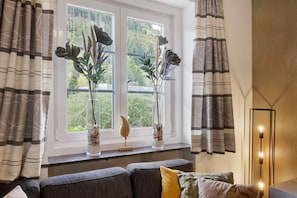 A room with a window, two vases with plants, a sofa with cushions, and a floor lamp.