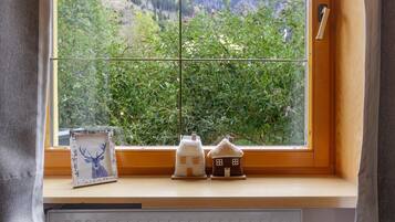 Una ventana con vista a un paisaje verde, un cuadro con un ciervo y dos casas pequeñas en el alféizar.