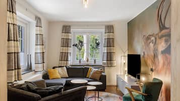 Ein modernes Wohnzimmer mit einer Couch, Sesseln, einem Couchtisch und einem Fernseher.