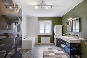 A modern bathroom with a bathtub, a large mirror, and a window.