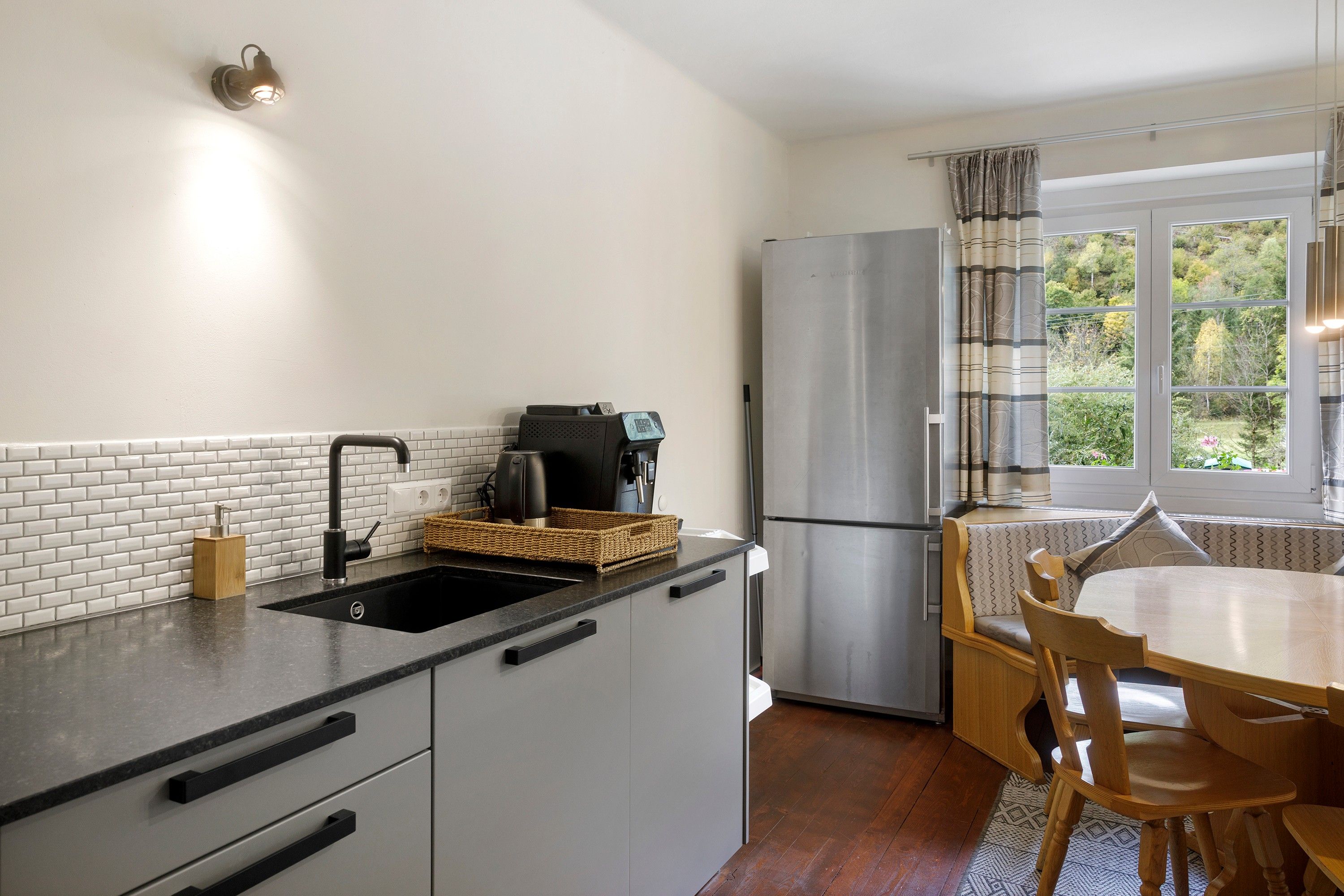 Una cocina compacta con un lavamanos negro, una cafetera, un refrigerador de acero inoxidable y una zona de comedor con mesa y sillas.